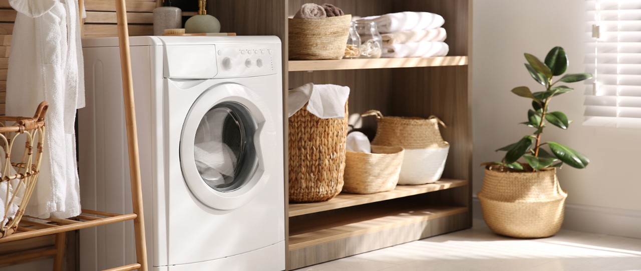 Dryer in laundry room next to shelves with folded towels and baskets.